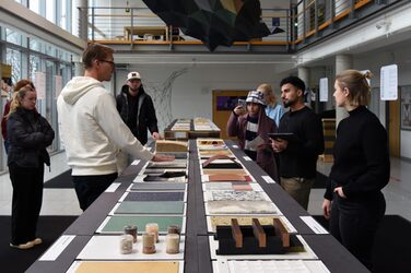 Der Mitarbeiter Daniel Horn erläutert einigen Studierenden Eigenschaften und Anwendungen einiger Materialien im Rahmen des Ausstellungsrundgangs