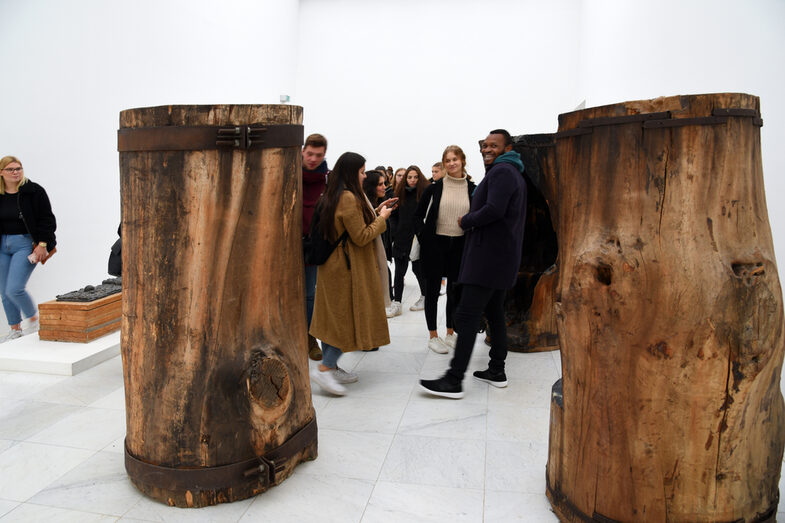 People stand in a gallery between tree trunks.