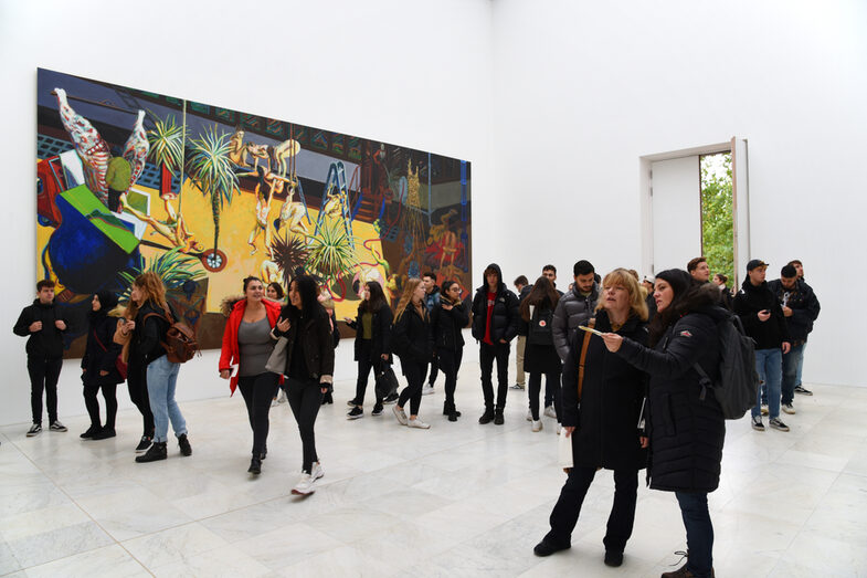 People walk through a gallery. There is a large painting in the background.