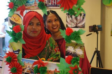2 female students in traditional dress look at us viewers through a decorated frame.