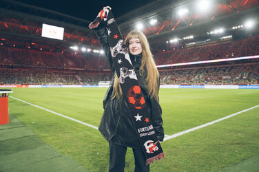 Eine Person steht am Spielfeldrand in einem Stadion und präsentiert einen Fanschal.
