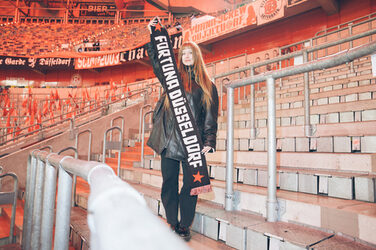 Eine Person steht am Spielfeldrand in einem Stadion und präsentiert einen Fanschal.