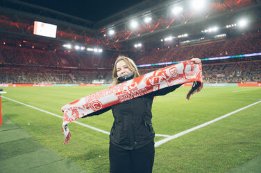 Eine Person steht am Spielfeldrand in einem Stadion und präsentiert einen Fanschal.