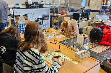 Vier Personen sitzen an einem Tisch und erstellen mit Stiften, an denen Kabel befestigt sind, Miniatur-Objekte.
