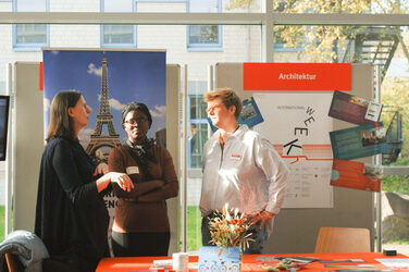 Drei Frauen in einem Gespräch an einem internationalen Messestand beim "Marktplatz der Möglichkeiten"__Three women in conversation at an international trade fair stand at the "Marketplace of Opportunities"