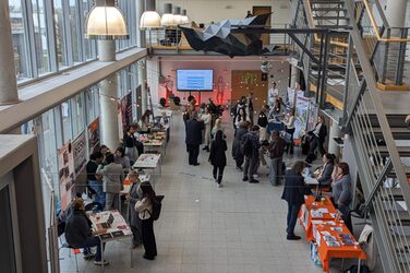 In einem Bereich des Foyers des Fachbereich Architektur der Fachhochschule Dortmun werden die Info-Talks beim International Day vorbereitet. Zu sehen ist der Präsentationsbildschirm und Stuhlreihen für das Publikum. In one area of the foyer of the Faculty of Architecture at Dortmund University of Applied Sciences, the info talks at the International Day are being prepared. You can see the presentation screen and rows of chairs for the audience.