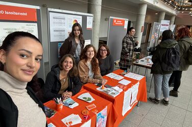 Drei Kolleginnen sitzen am Messestand des International Office beim international Day. Three colleagues sit at the International Office exhibitor's stand at the International Day.