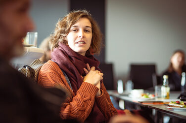 Frau mit Schal und orangenem Strickpullover spricht mit einem Mann in der Unschärfe links__Woman with scarf and orange knitted sweater talking with man in blur on left