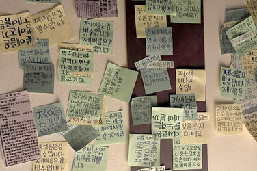 Several dozen Post-It notes with Korean characters hang on a wall.