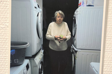 A person stands between washing machines and dryers and looks into the camera.
