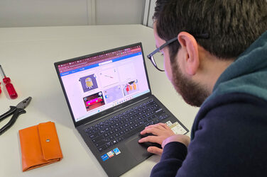 Eine Person bedient einen Laptop, auf dem Bildschirm sind mehrere Motive einer Bilddatenbank zu sehen. Daneben liegt Werkzeug.