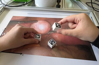 Auf dem Foto von einer Operation liegen Würfel mit QR-Codes, zwei Hände greifen nach den Würfeln.