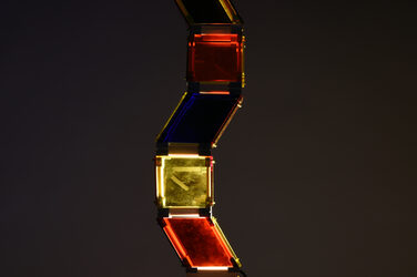 Night shot of a colorfully illuminated, sculptural lamp on a wooden base