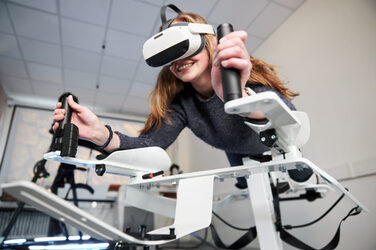 Foto von einer Person auf dem Icaros-Gerät. Sie trägt eine VR-Brille und hält sich an den Griffen fest.