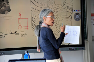 Die Gast-Professorin aus Bali vor einem mit Entwurfsskizzen bespieltem Monitor.