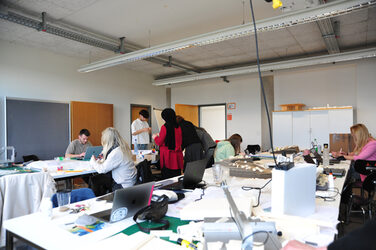 Studierende arbeiten gemeinsam in einem Projektraum an Modellen und Laptops.