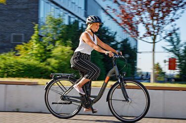 Photo of a young woman riding a bike across campus. She is wearing a helmet __ Young woman rides a bike across campus.