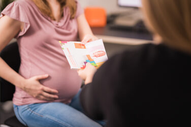 Photo of a pregnant woman sitting across from a Family Service employee accepting some flyers on the topic of "Reconciling family and career." __Photo of a pregnant woman sitting across from a Family Service employee accepting some flyers on the topic of "Reconciling family and career."