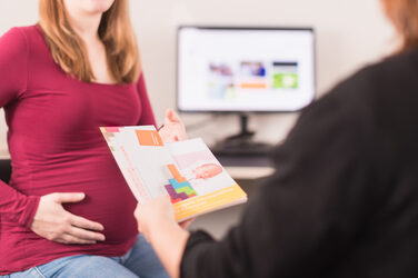 Photo of a pregnant woman sitting opposite an employee from the Family Service and taking some flyers on the subject of "Reconciling family and studies".