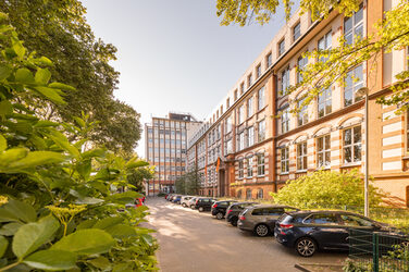 Photo of the old building and the high-rise on Sonnenstrasse with the parking lot in front of it. A flowering bush in the left-hand section of the picture.