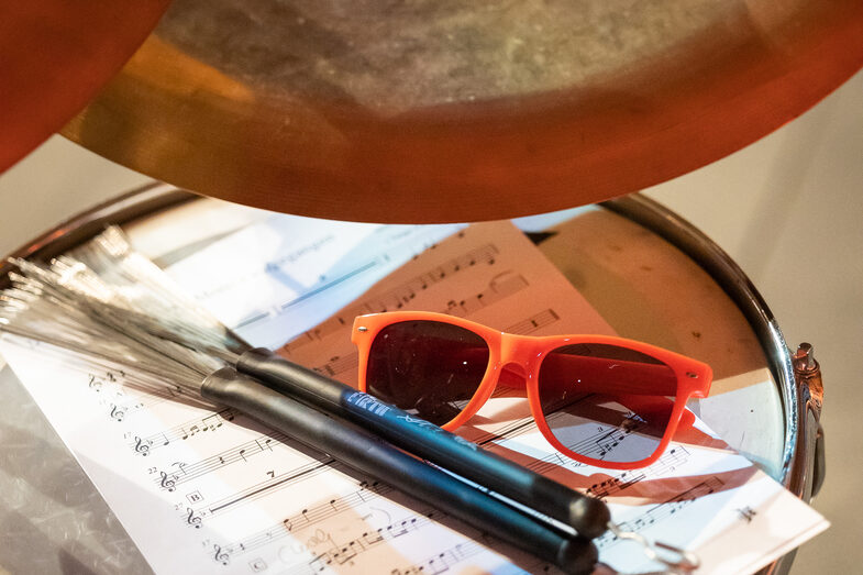 Foto eines Schlagzeugs. Auf diesem liegen ein Notenblatt, eine Sonnenbrille und zwei Drumsticks.