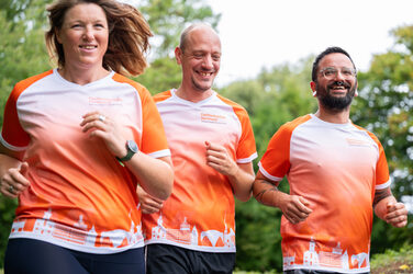 Drei Personen in FH-Dortmund-Laufshirt laufen im Grünen, man sieht nur die Oberkörper und Gesichter.