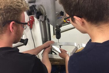 Two students drill holes in parts of their railing using a drill press.