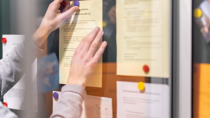 Photo of a display case with several notes pinned inside. One person pins up another piece of paper with magnets.