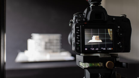 Photo of a camera screen pointing at a model of a building against a black background.