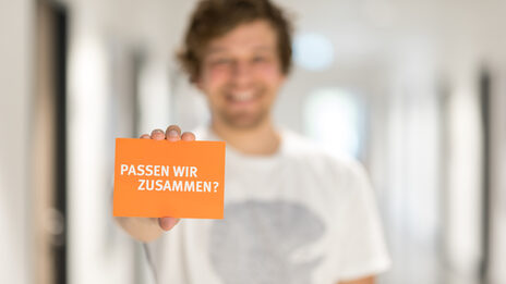 Photo of a man holding a card with the words "Do we fit together?" into the camera __Man out of focus holding a card with the words "Do we fit together?" into the camera.