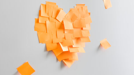 Photo of a heart stuck together from orange sticky notes on the wall. __ A heart stuck together from orange sticky notes on the wall.