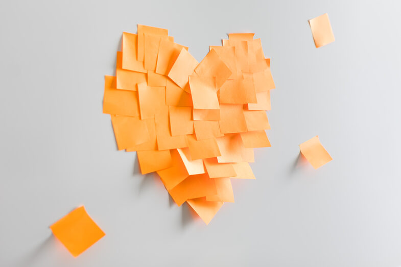 A heart glued together from orange sticky notes on the wall.