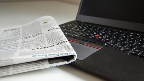 Photo of a folded newspaper lying on the keyboard of a laptop.