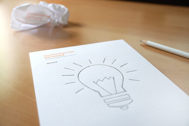 Photo of a sketch of a light bulb on a FH block, crumpled paper in the background and a FH pencil. __ Sketch of a light bulb on a FH block, crumpled paper in the background and a FH pencil.