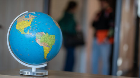 Photo of a globe on a table. In the background you can see students talking.