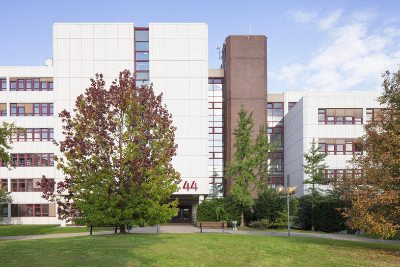 Photo of the building Emil-Figge-Straße 44 of the Fachhochschule Dortmund, in front of it green space and trees.