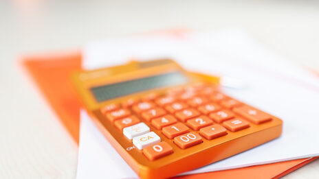 Photo of an orange pocket calculator lying on an orange folder and a pile of notes.