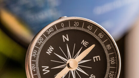 Photo of a compass, in the background a very blurred globe.