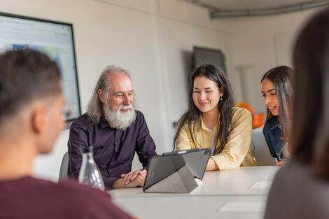 International students and a lecturer at an International Career Service workshop are sitting at a table looking at a tablet.