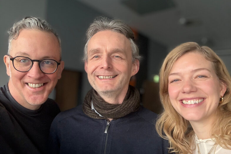 Three people can be seen with head and upper body, standing next to each other and looking friendly into the camera.