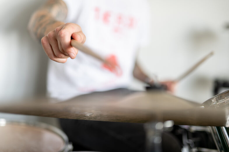 Close-up of a drum cymbal and a man's arm hitting the cymbal with a stick.