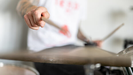 Close-up of a drum cymbal and a man's arm hitting the cymbal with a stick.