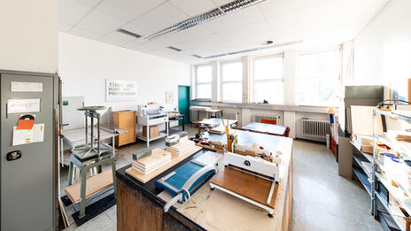 Photograph of the paper workshop. In addition to cupboards, shelves and tables, there is a lot of equipment here that is needed for paper processing/bookbinding.