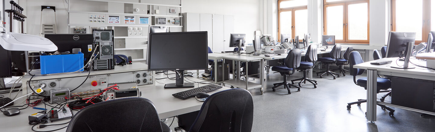 Hier sieht man weitere Arbeitsplätze und den schon zuvor beschrieben Arbeitsplatz mit dem aufgebauten Versucht, sieht man rechts hinten. Bei dem vordersten Arbeitsplatz auf dem Bild kann man einen weiteren Versuchsaufbau erkennen.