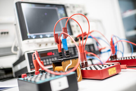 A photo of an experimental setup. A sweep generator feeds a voltage divider with a parallel resonant circuit. In front of the generator there is an R decade, a coil with a parallel C decade plus a diode and another capacitor to smooth the voltage. There is an oscilloscope in the background.