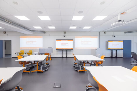 Room shot of the InnoLab, part of the room is shown here, with a view across group work tables to projector surfaces and digital whiteboards.