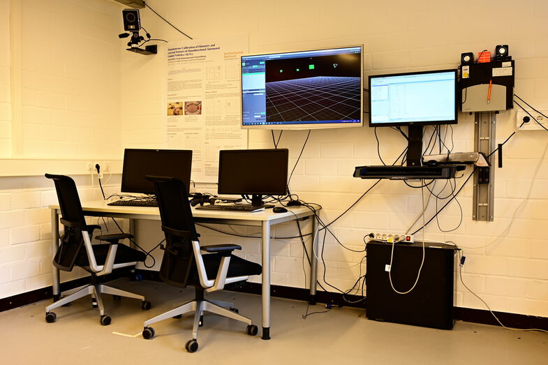 Zwei Stühle und ein Schreibtisch mit Computern und mehreren Bildschirmen__Two chairs and a desk with computers and several screens