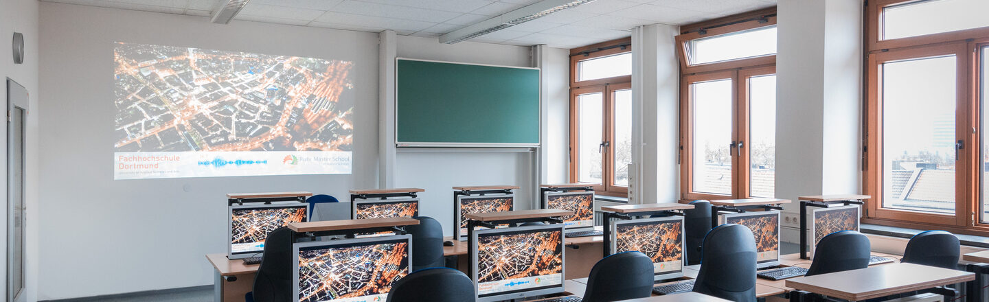 Room shot of a laboratory in the Faculty of Information Technology with rows of seats and PCs. Something is beamed onto the wall of the room.