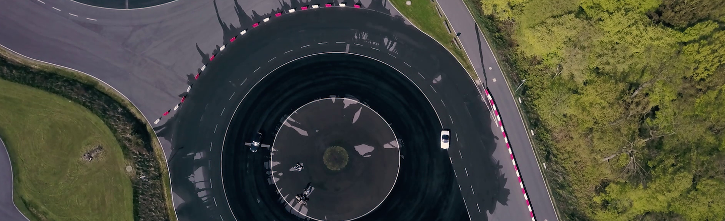 Bird's eye view of a circular track with irrigation. Test vehicles (Volvo, Spyder) are driving on it.