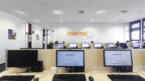 Photo of several computer workstations in the library reading room, some of them used by students__Photo of the computers in the library reading room, some of them used by students